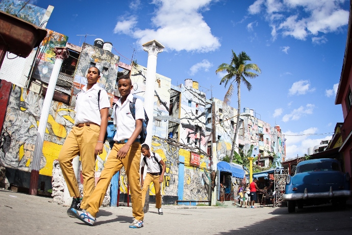 Dois jovens com uniformes escolares caminham em uma rua ensolarada de Havana.